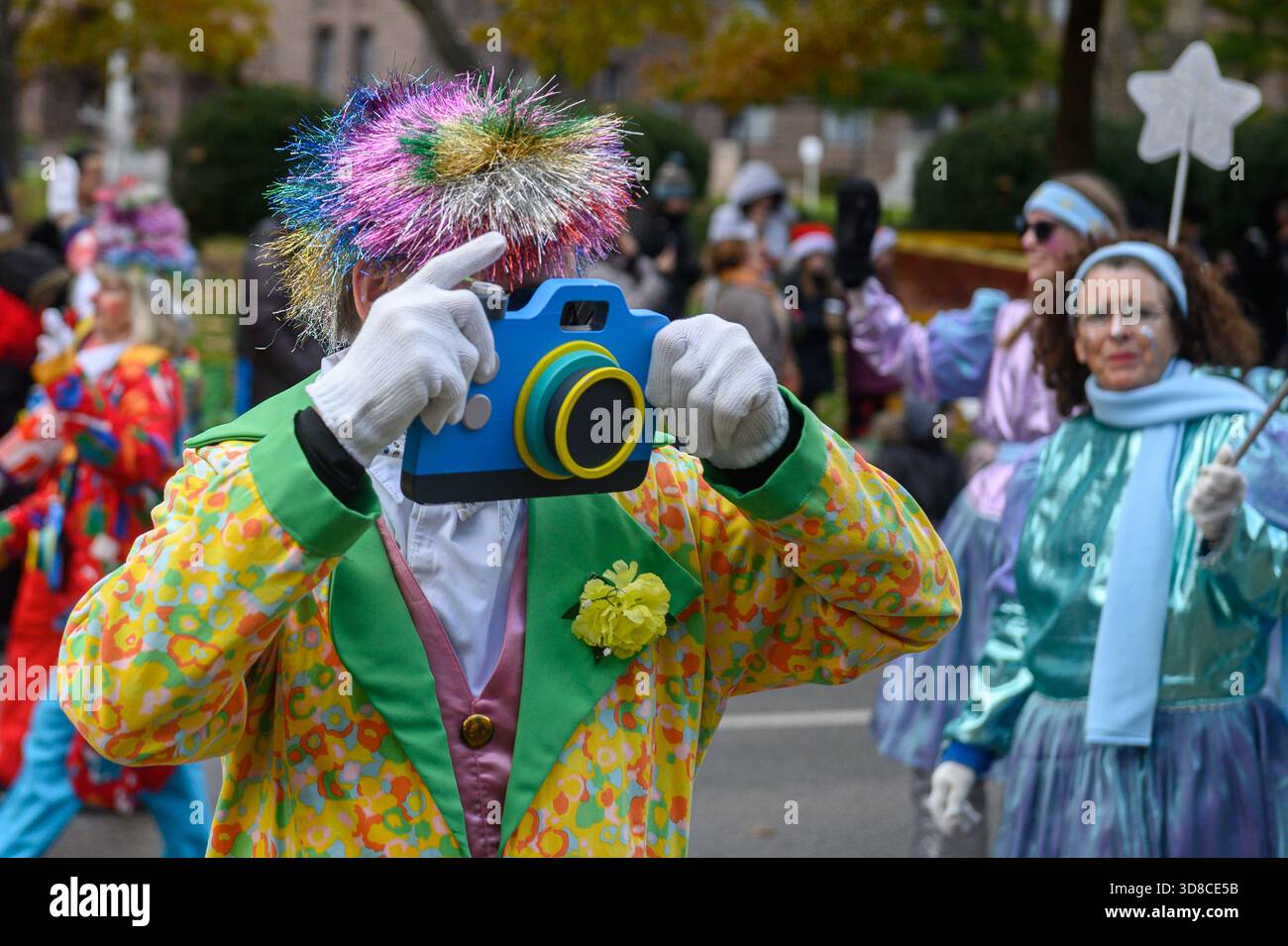 TORONTO, ONTARIO, CANADA - 23 NOVEMBRE 2025: Un Celebrity Clown che indossa una colorata giacca a pois e una parrucca arcobaleno tiene in mano un nuovo supporto per la fotocamera Foto Stock