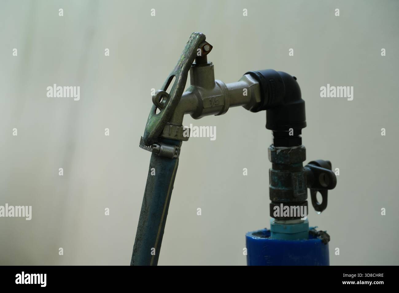 Un vecchio rubinetto all'aperto con un tubo collegato mostra l'età e gli agenti atmosferici, sollevando domande sulla conservazione dell'acqua e sulla gestione sostenibile delle risorse Foto Stock