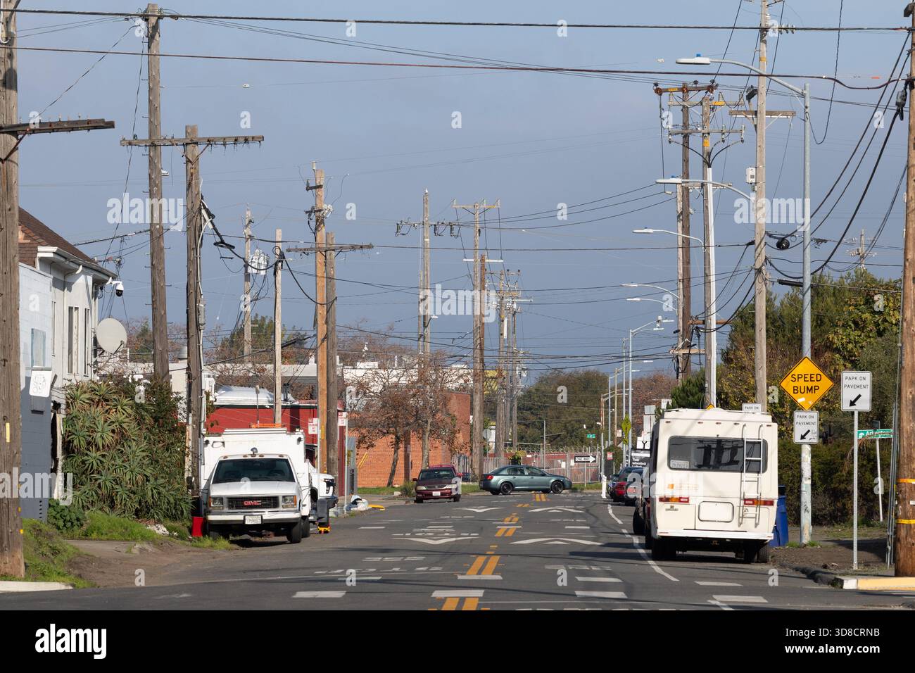 Pali e linee elettriche dominano la vista lungo una tranquilla Oakland Street, dove i veicoli parcheggiati fiancheggiano la strada sotto la chiara luce del pomeriggio. Foto Stock