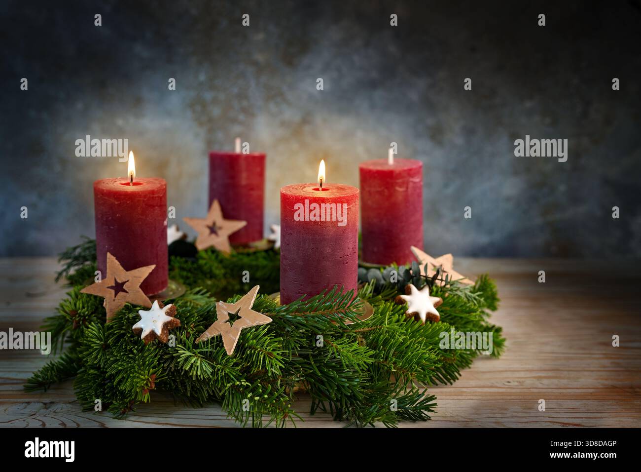 Quattro candele rosse su una corona dell'Avvento, due accese per il secondo avvento, piccole stelle e biscotti alla cannella come decorazioni natalizie, sfondo bluastro, Foto Stock