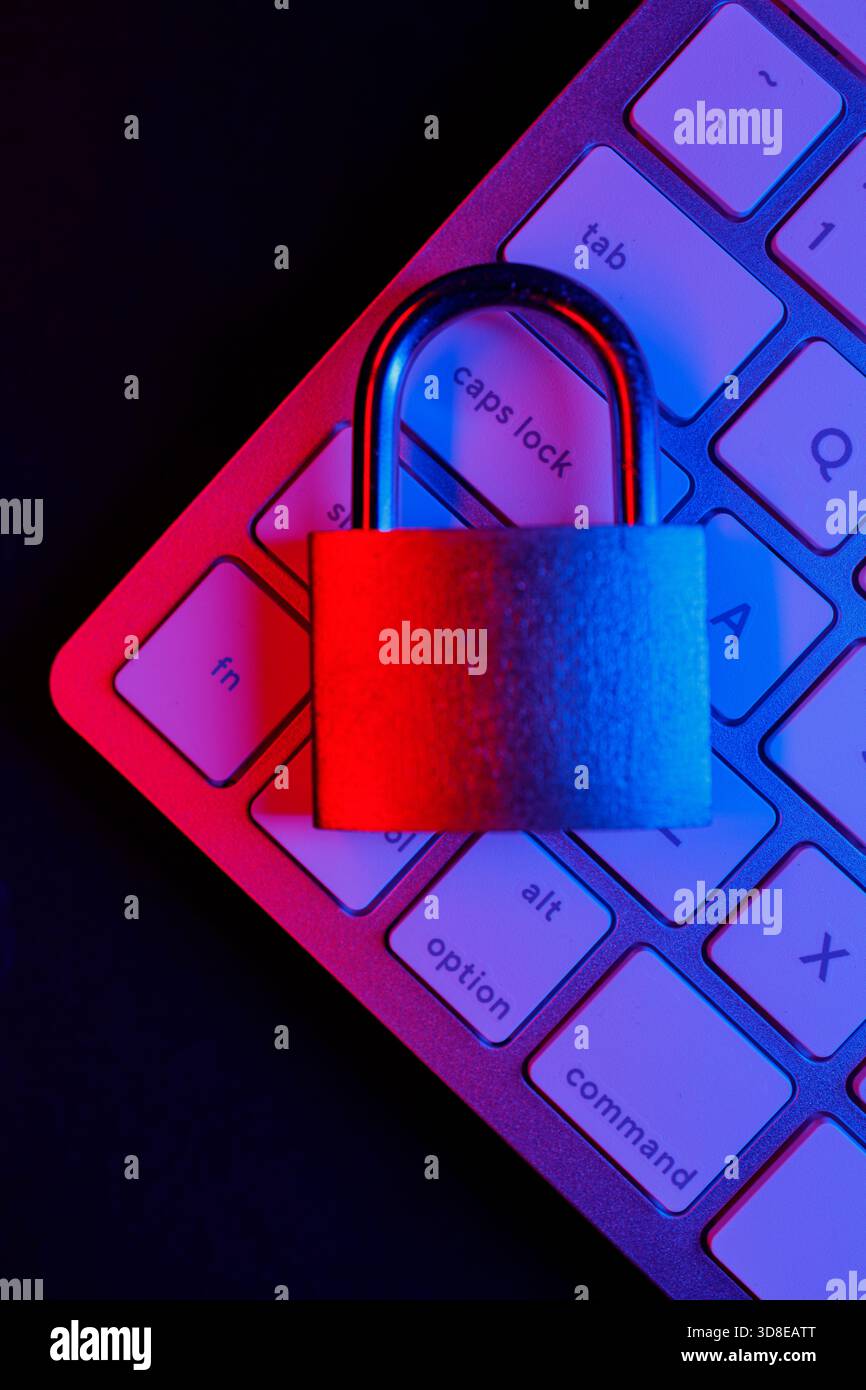 Un robusto lucchetto è posizionato sulla tastiera di un computer, illuminato da luci blu e rosse. Questa scena evidenzia l'importanza di Internet Securi Foto Stock