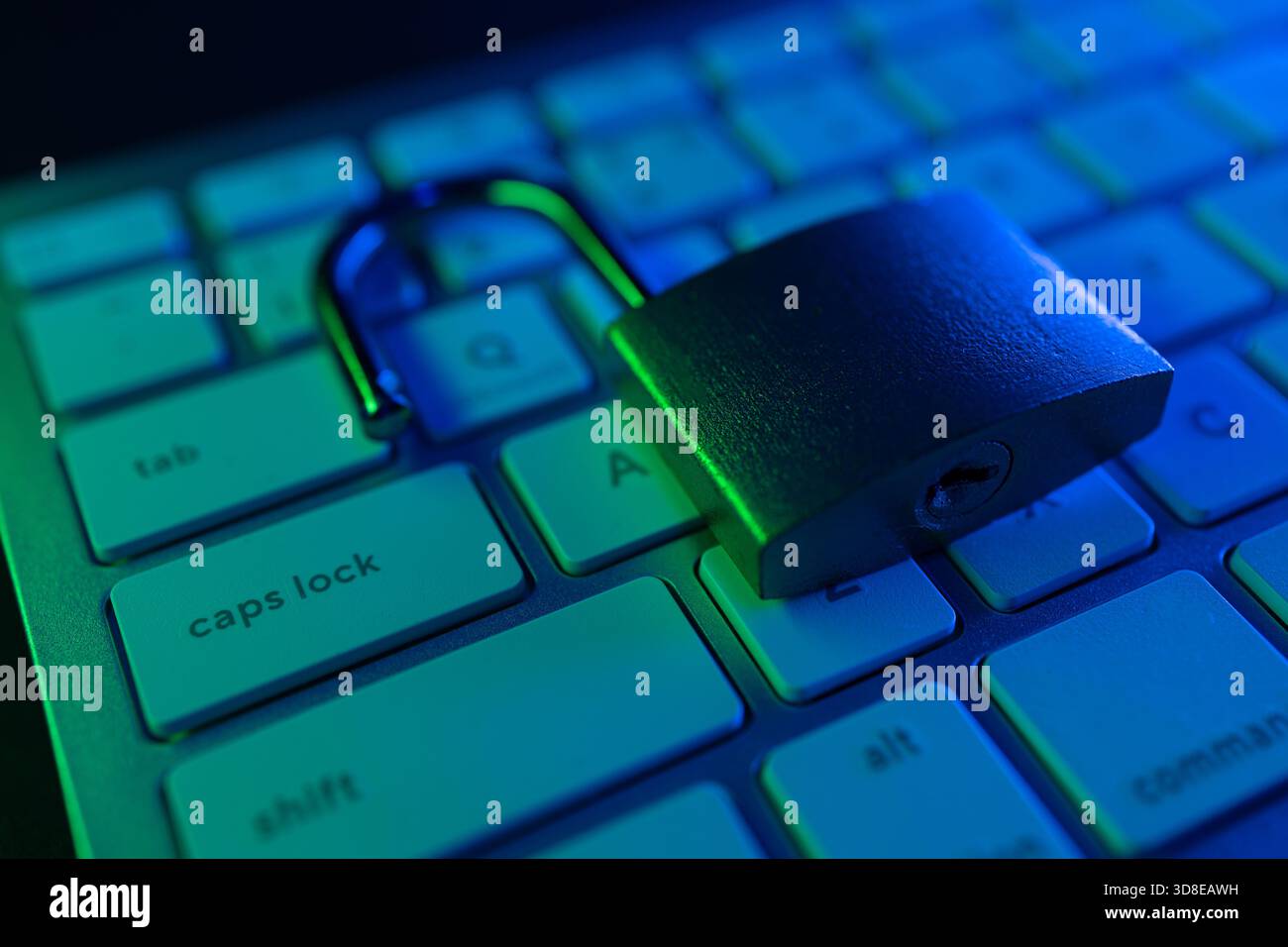 Un lucchetto metallico è sbloccato sulla tastiera di un computer illuminato da una spia blu-verde. Questa scena simboleggia le sfide nella sicurezza informatica e nella salvaguardia Foto Stock