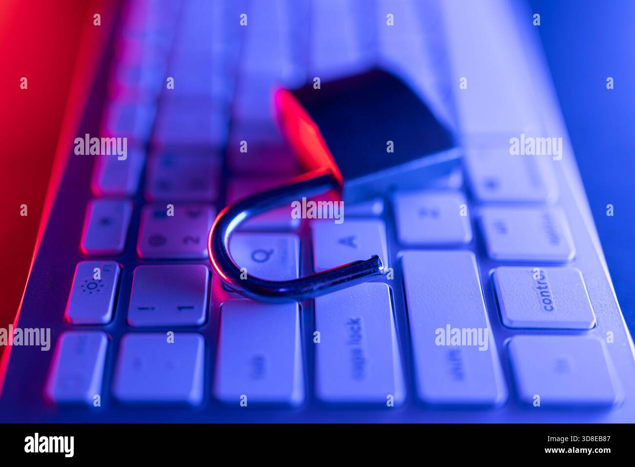 Un lucchetto viene posizionato sulla tastiera di un computer, a simboleggiare l'importanza della sicurezza informatica. La scena è illuminata con luci blu e rosse, enfasi Foto Stock