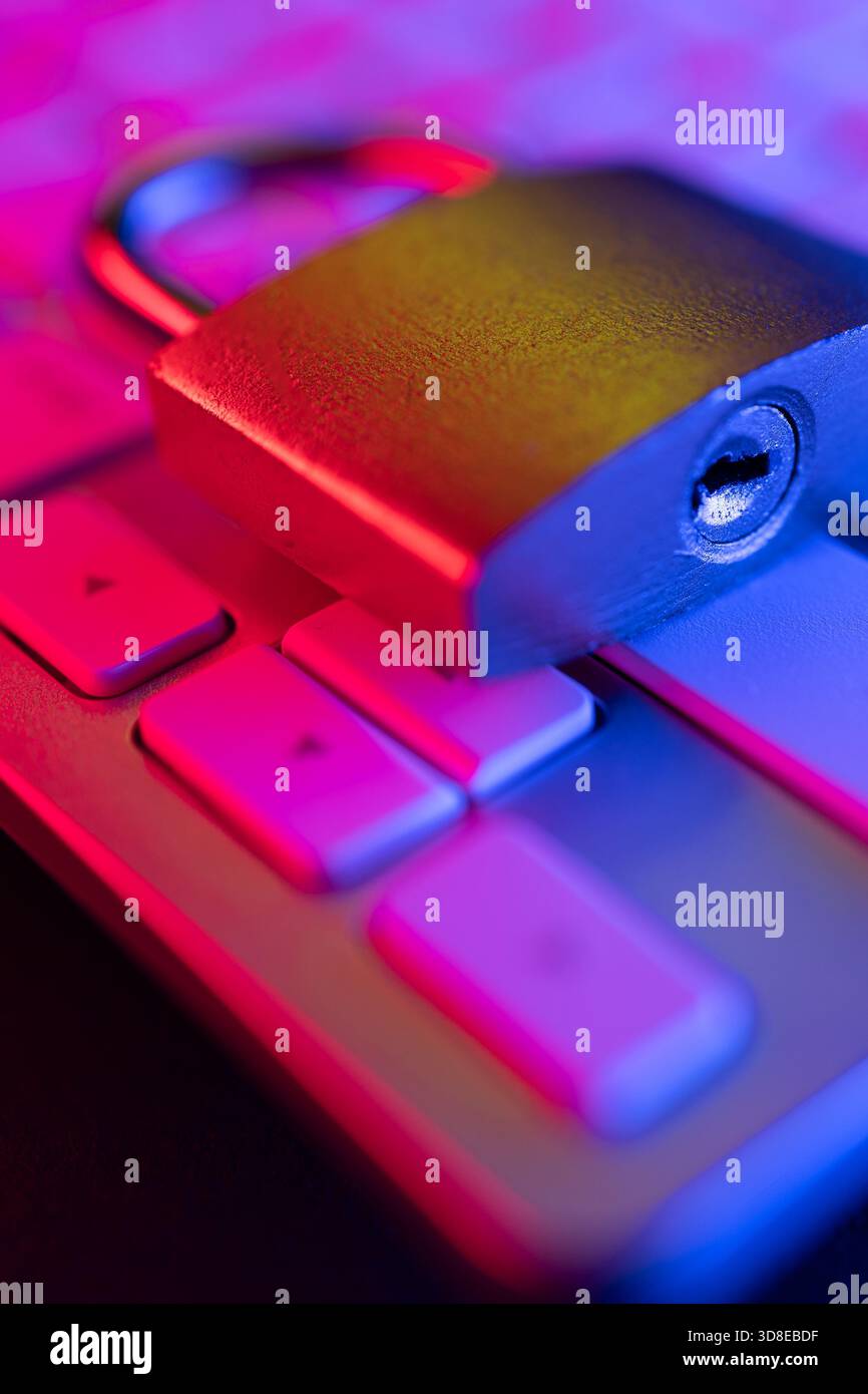 Una serratura a combinazione è posizionata su una tastiera del computer illuminata da un'illuminazione colorata. Questa scena evidenzia l'importanza della sicurezza informatica nella protezione Foto Stock