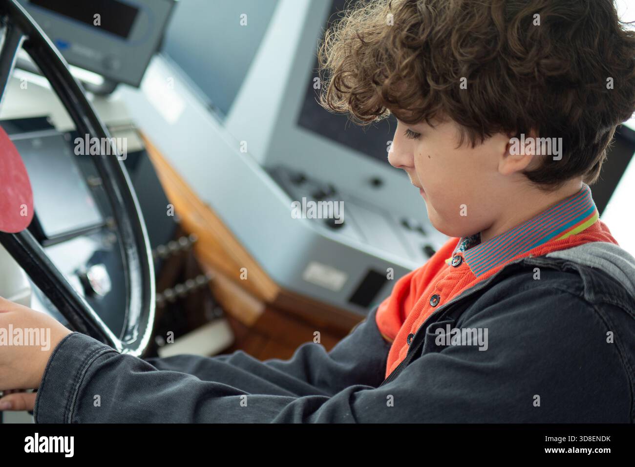 Bambino che utilizza una ruota di controllo storica all'interno di un'imbarcazione o ambientazione storica, illustrando l'apprendimento pratico e l'istruzione attraverso l'esperienza. Foto Stock