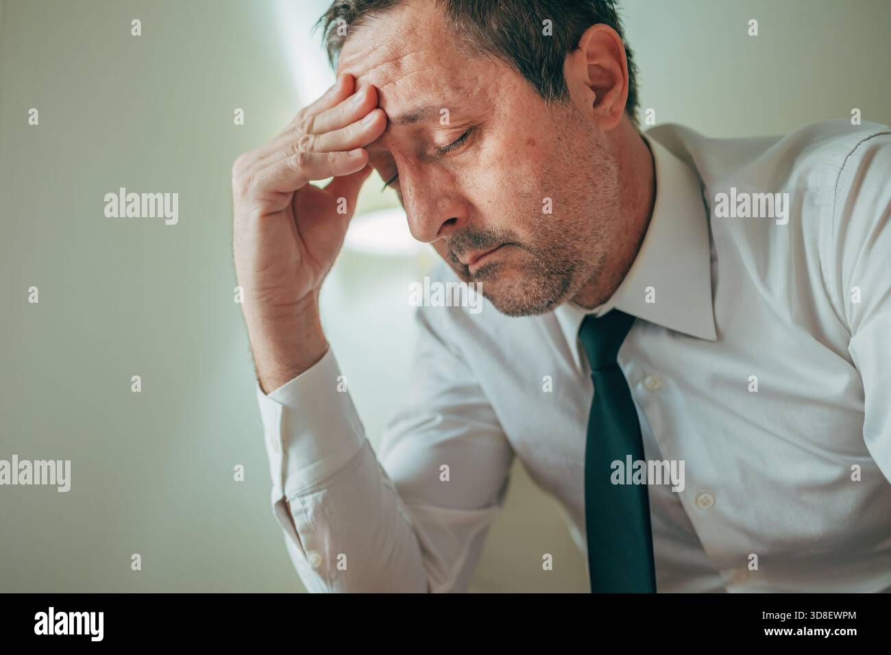 Uomo d'affari stanco e turbato con una mano sulla fronte, che si sente sopraffatto dallo stress e dalla fatica. Messa a fuoco selettiva. Foto Stock