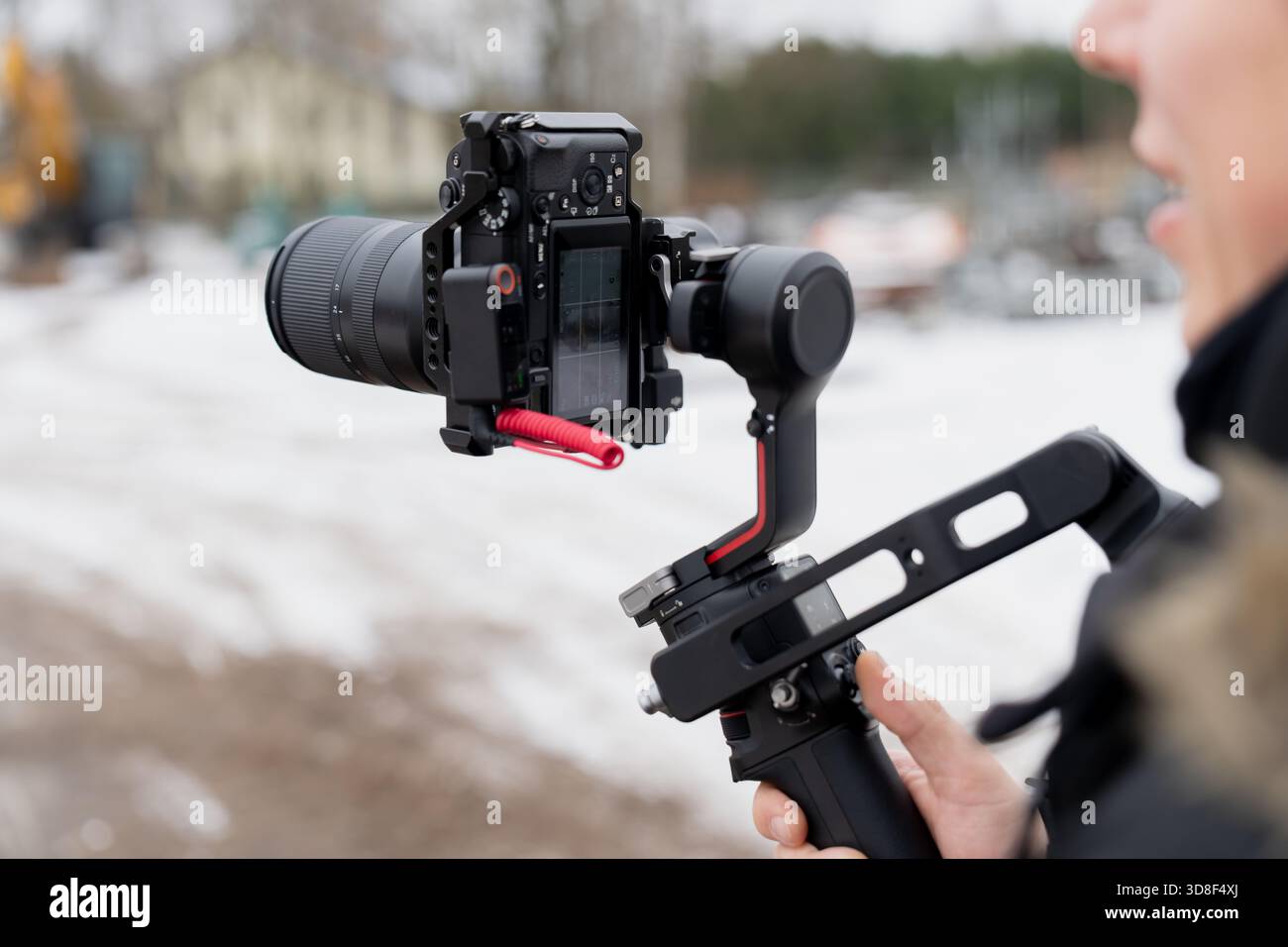 Operatore video che utilizza una fotocamera mirrorless montata su uno stabilizzatore cardanico per acquisire riprese stabili in condizioni di lavoro esterne fredde Foto Stock