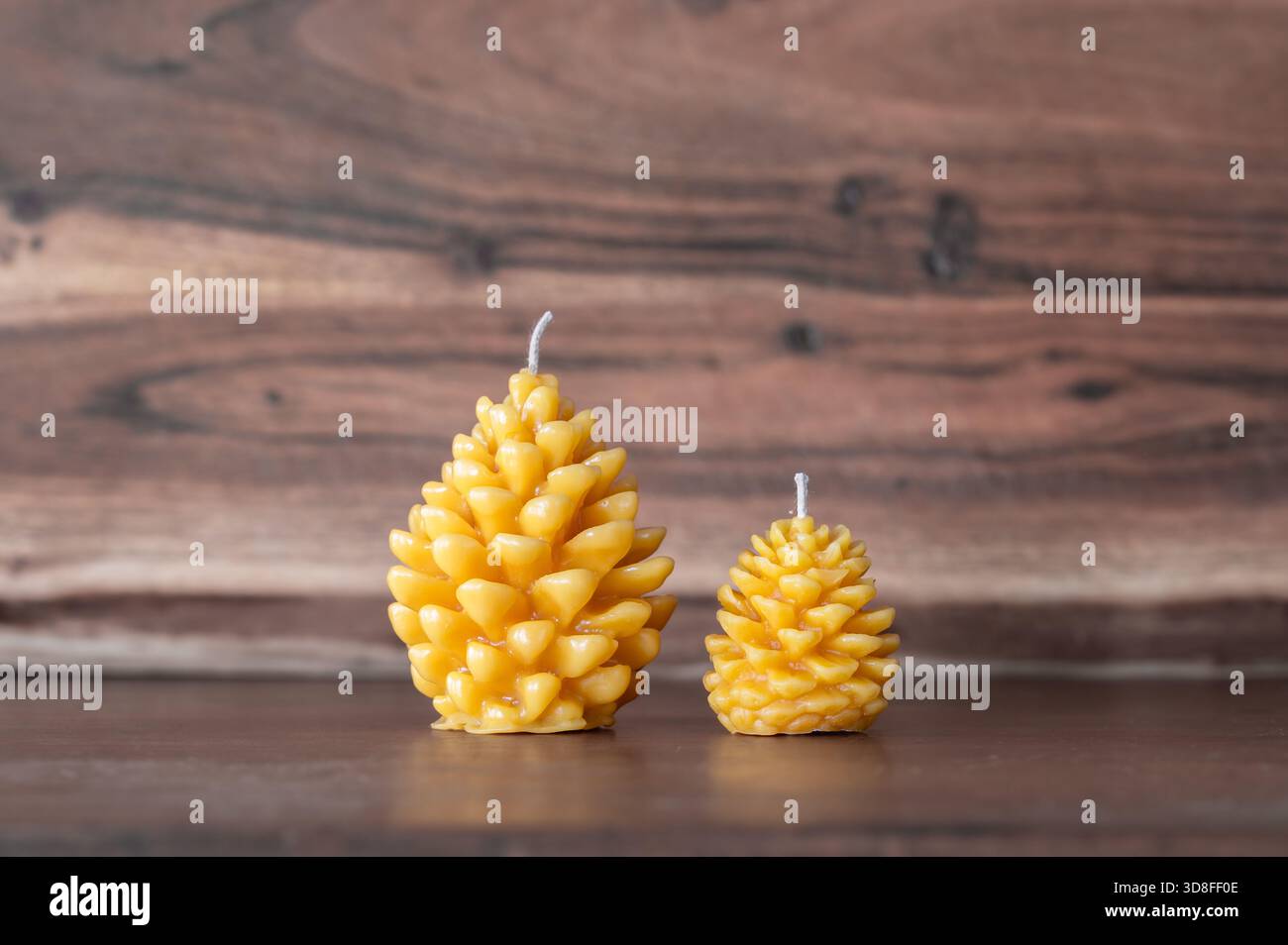 Due candele a cono di pino in cera d'api, una grande e piccola, fondo in legno Foto Stock