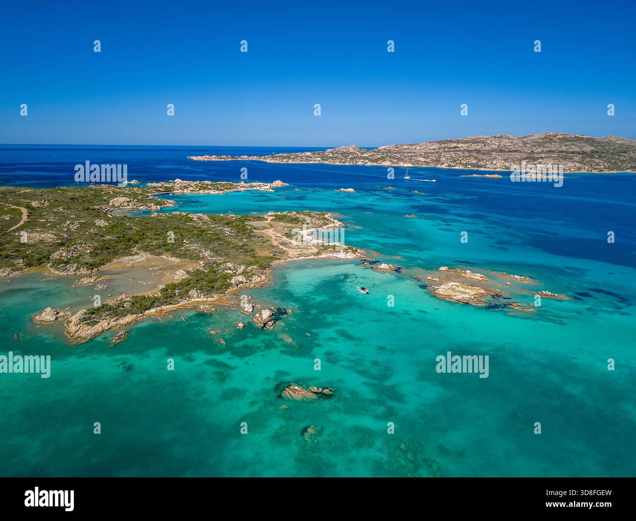 Panorama costiero aereo caratterizzato da acque turchesi poco profonde, insenature rocciose e una lontana cresta isolana, Sardegna, Italia Foto Stock