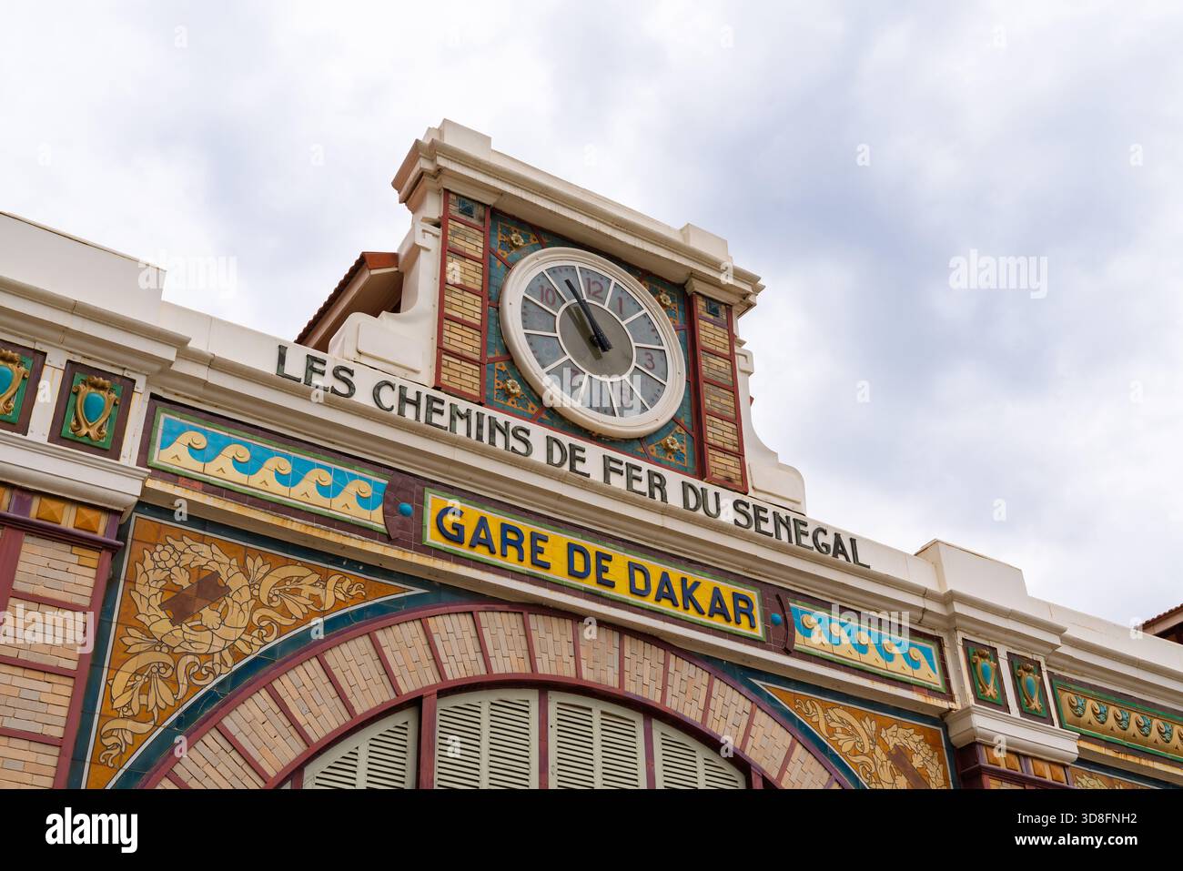 Dakar, Senegal. 11 novembre 2025. La colorata facciata coloniale e l'orologio della stazione ferroviaria Gare de Dakar si affacciano dalla strada Foto Stock