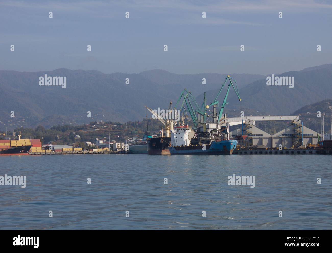 Porto marittimo commerciale con navi da carico e gru lungo la costa montana Foto Stock