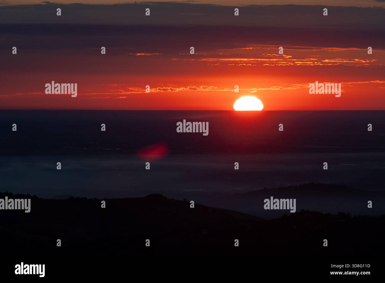 La Pianura Padana all'alba di luglio, con nebbia, nuvole e il disco rosso del sole nascente Foto Stock