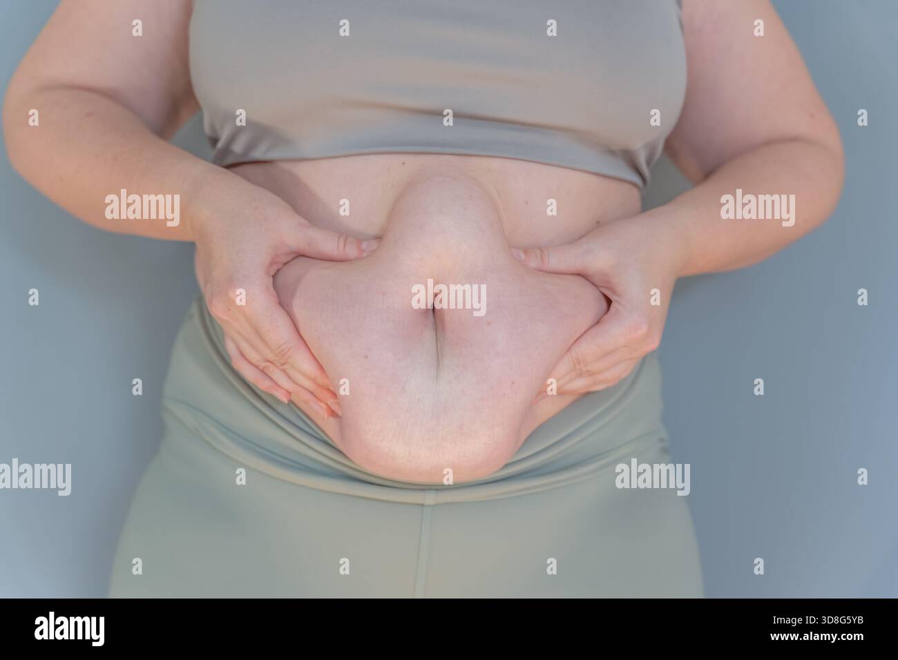 Donna che tiene il grasso della pancia con entrambe le mani, la pelle sciolta e il grasso addominale primo piano Foto Stock