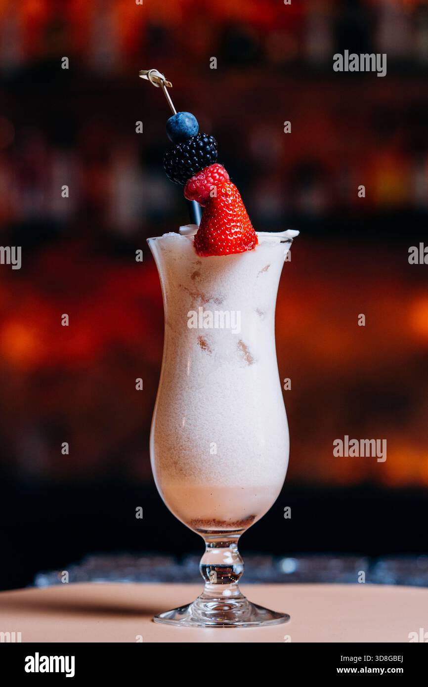 Bevanda cremosa e miscelata servita in un alto vetro curvo con sfumature di cioccolato o caffè, condita da un vivace spiedino di frutti di bosco freschi Foto Stock