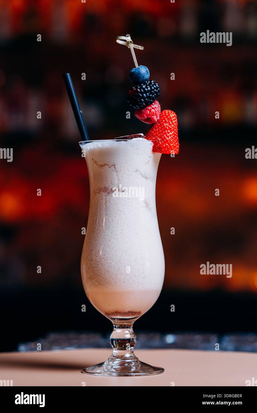Bevanda cremosa e miscelata servita in un alto vetro curvo con sfumature di cioccolato o caffè, condita da un vivace spiedino di frutti di bosco freschi Foto Stock