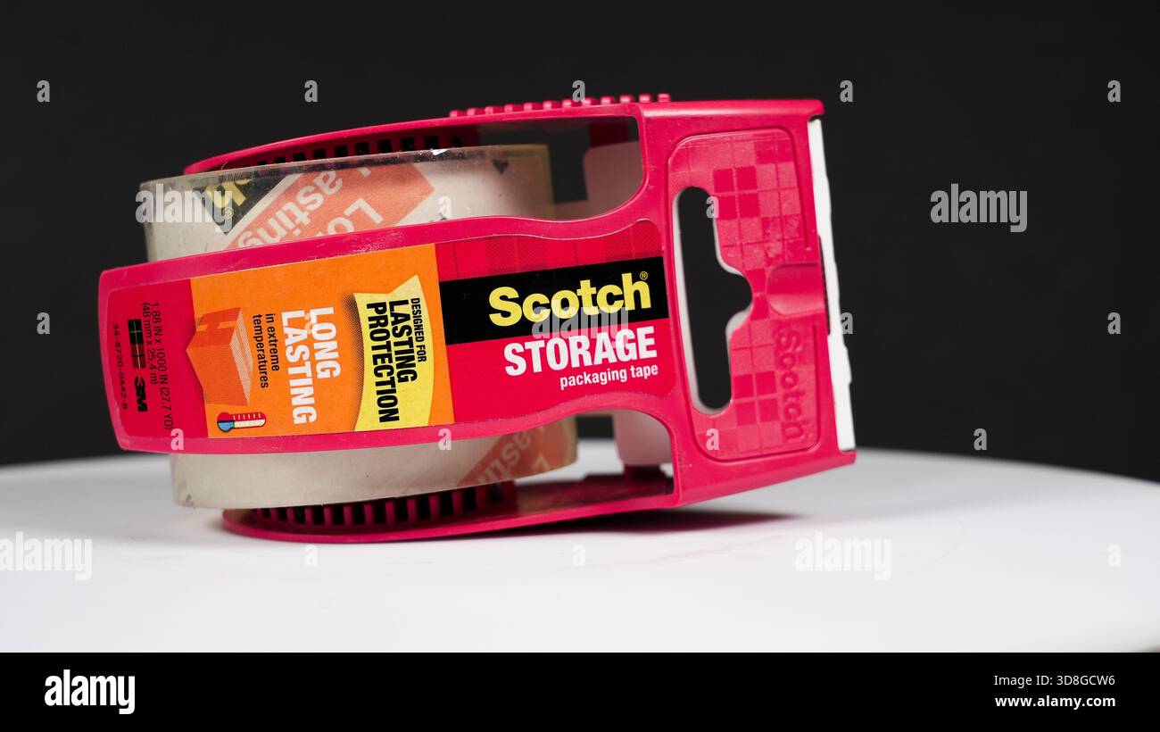 NORWALK, CT, USA- 19 FEBBRAIO 2025: Un dispenser di nastro per imballaggio rosso brillante si trova su una superficie bianca semplice, sottolineandone i colori vivaci e la praticità Foto Stock