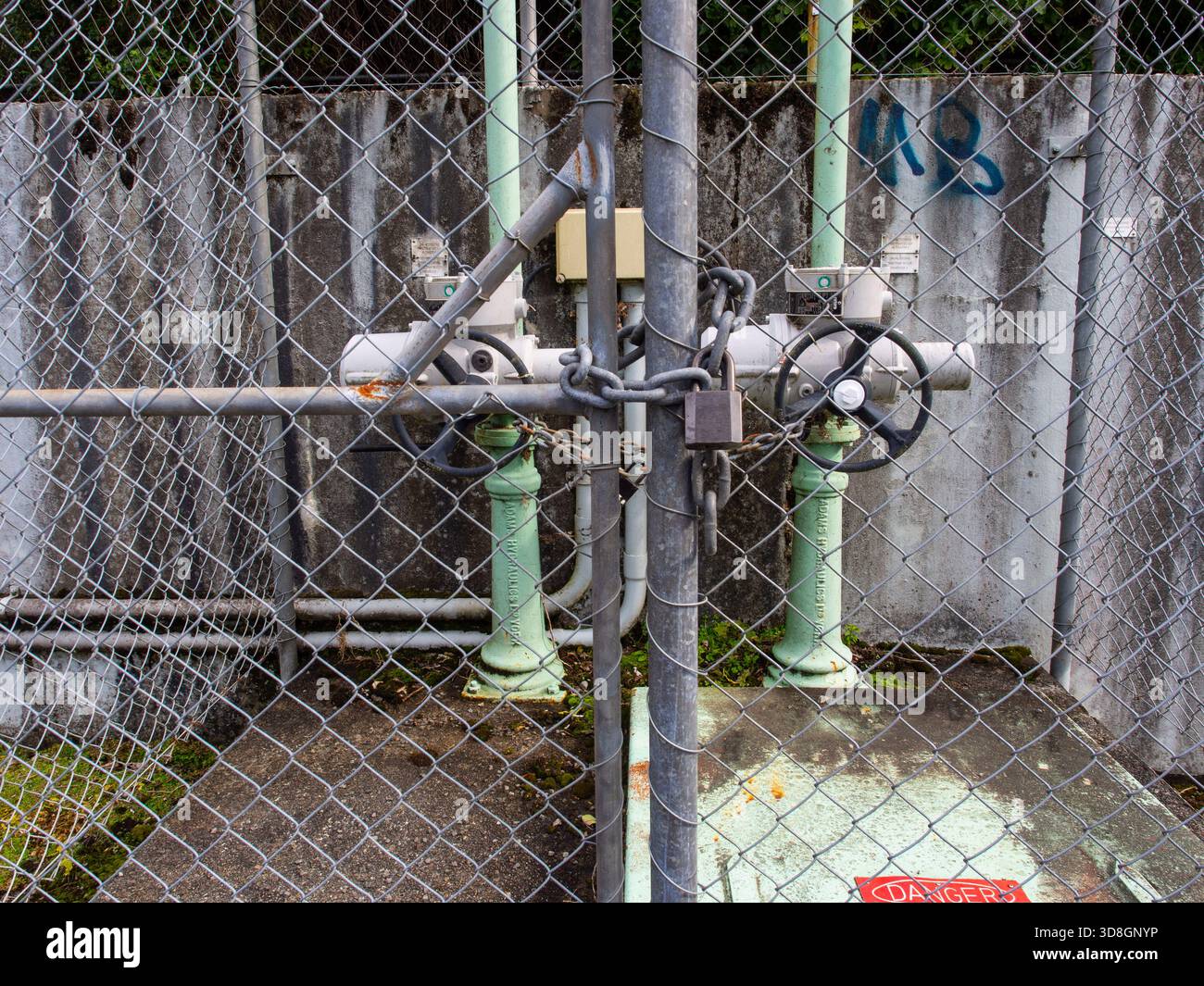 Cancello a maglie a catena con lucchetto che fissa le valvole per impianti idrici industriali e l'infrastruttura di servizi pubblici Foto Stock