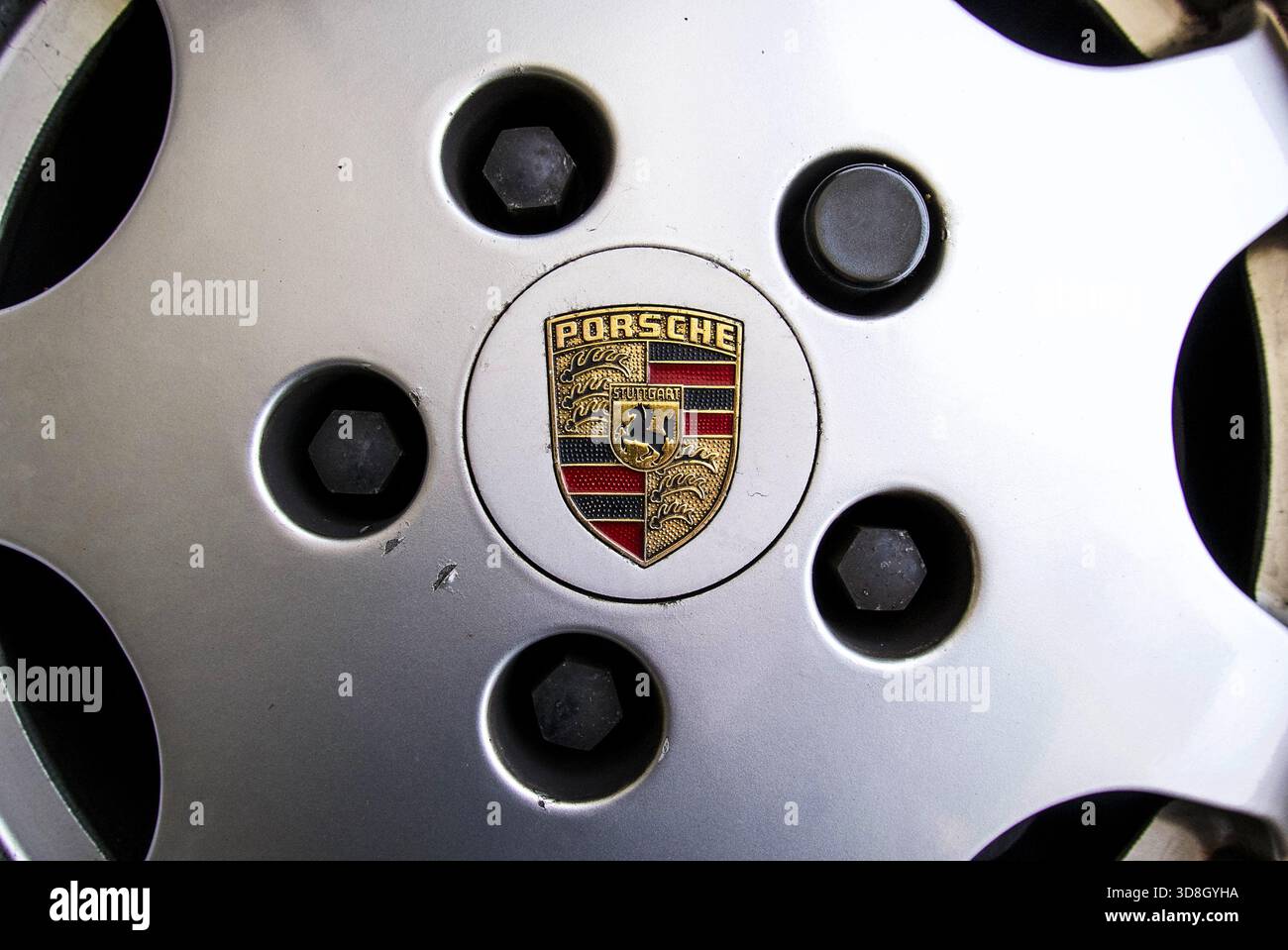 Primo piano dello stemma Porsche al centro di un cerchio in lega verniciato in argento, con un piccolo frammento di vernice Foto Stock