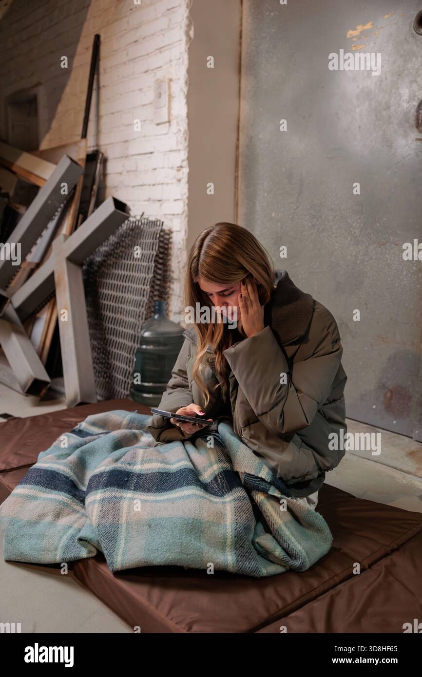 Donna che legge notizie al telefono nel rifugio antiatomico. Guerra in Ucraina. La vita in una stazione della metropolitana di un rifugio antiatomico. Donna che legge notizie sul cellulare Foto Stock