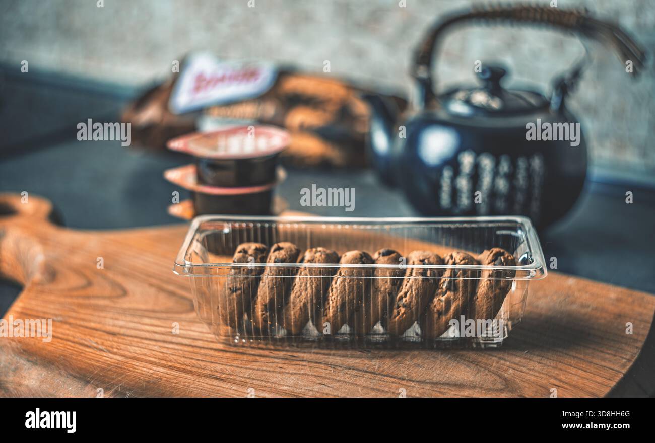 Un semplice rituale del tè casalingo con una teiera di argilla, biscotti freschi e marmellata ben posizionata su un tavolo da cucina in legno in una luce soffusa naturale Foto Stock