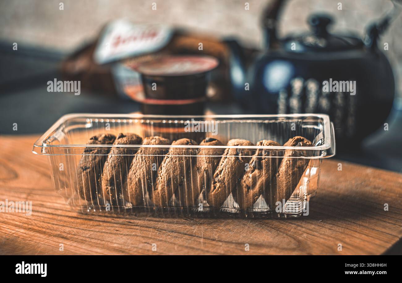 Un momento rustico per il tè in cucina: Teiera di argilla nera, biscotti croccanti e marmellata in porzioni su un tavolo di legno in luce dolce Foto Stock