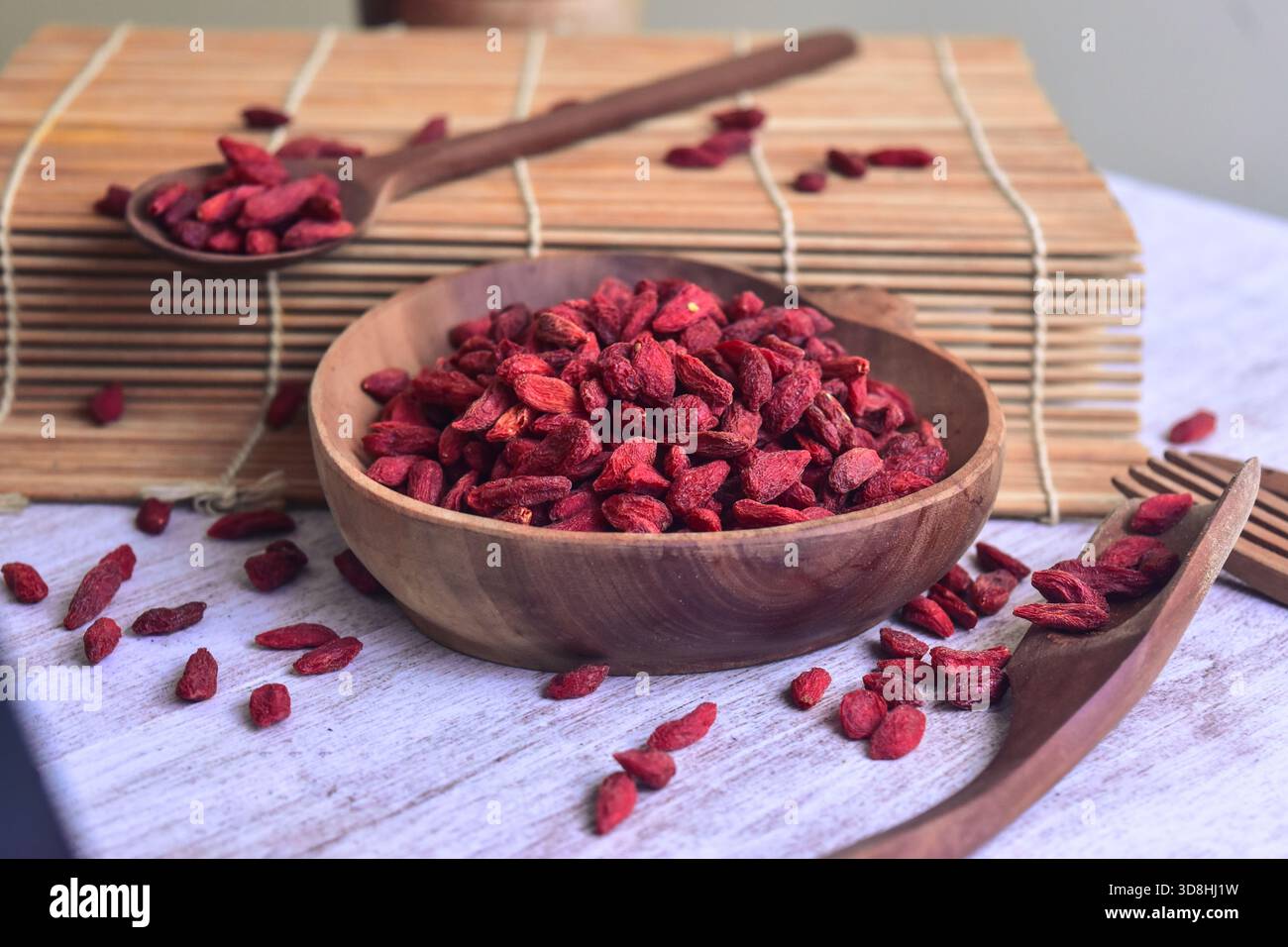Bacca di goji essiccata all'interno di una ciotola di legno sul lato del rullo per sushi con cucchiai di legno e forchetta sul lato superiore del tavolo Foto Stock