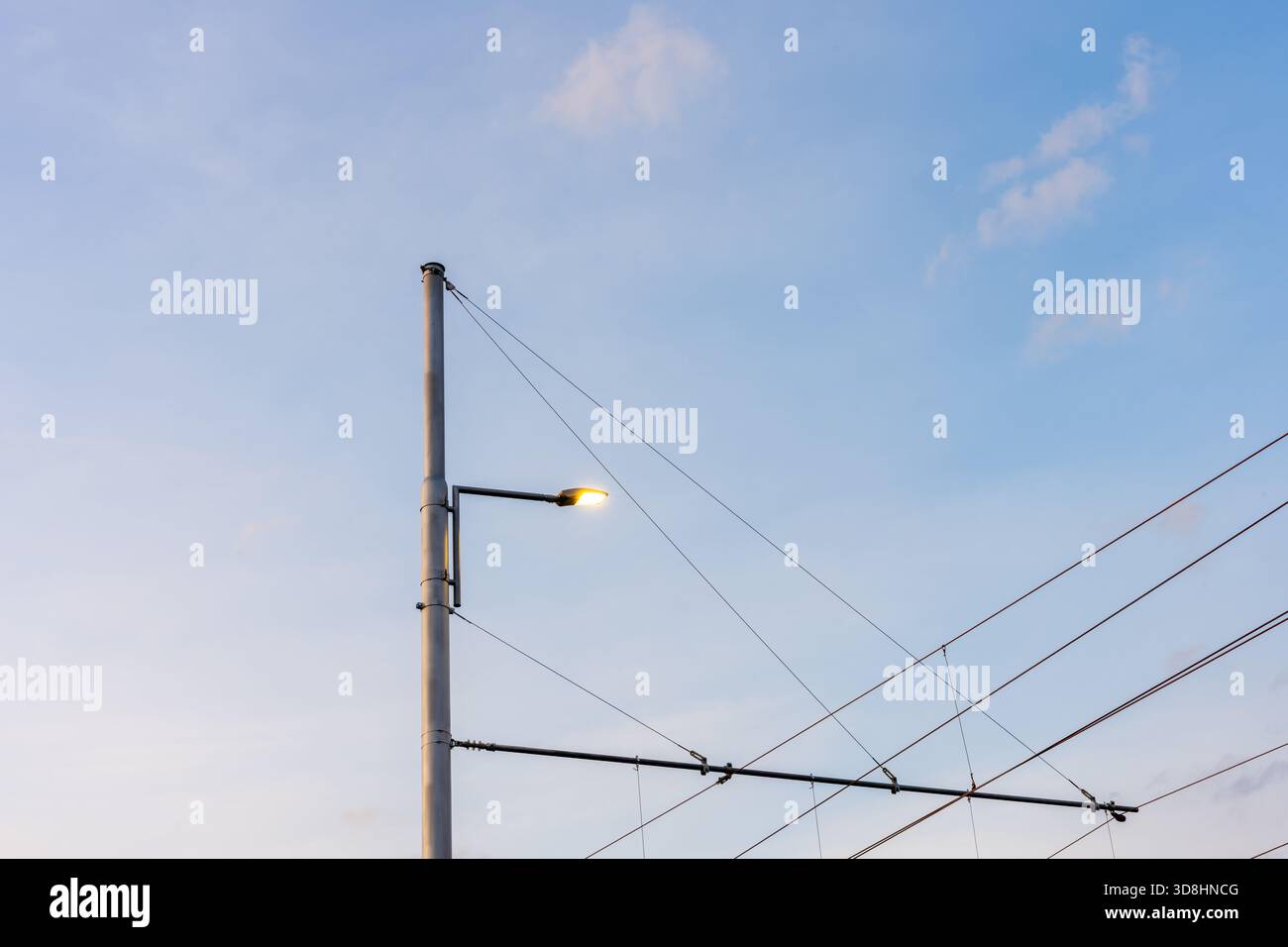 Lampioni stradali e cavi del tram sopraelevati contro il cielo blu morbido nelle infrastrutture di trasporto urbano Foto Stock