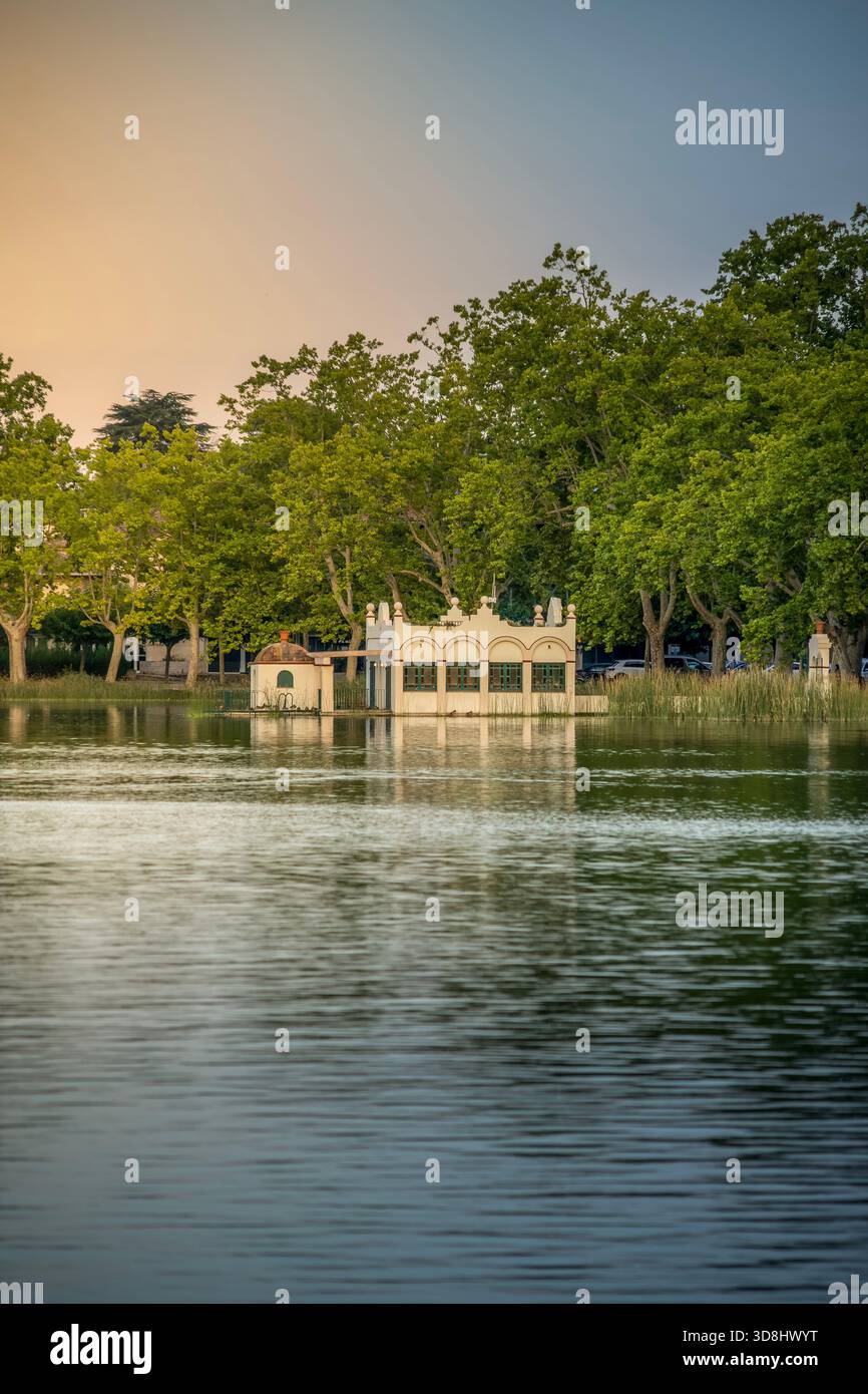 La storica struttura Pesqueres de Banyoles (Case dei pescatori) sull'acqua, circondata da vibranti alberi verdi sul lago Banyoles, in Spagna Foto Stock