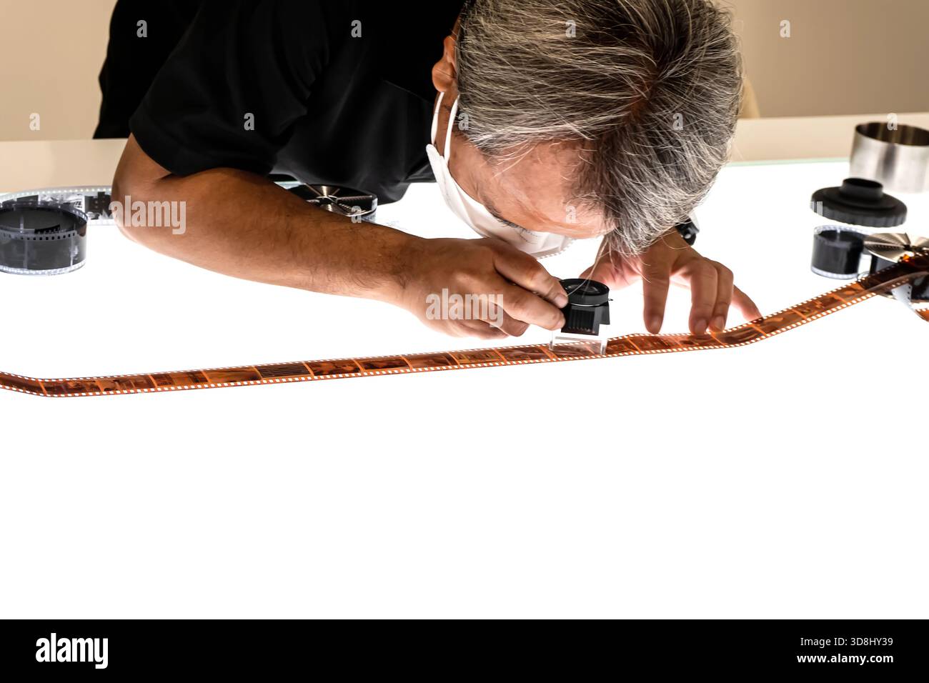 Un uomo che esamina da vicino una striscia di pellicola a colori sviluppata sotto ingrandimento su uno sfondo bianco. Foto Stock