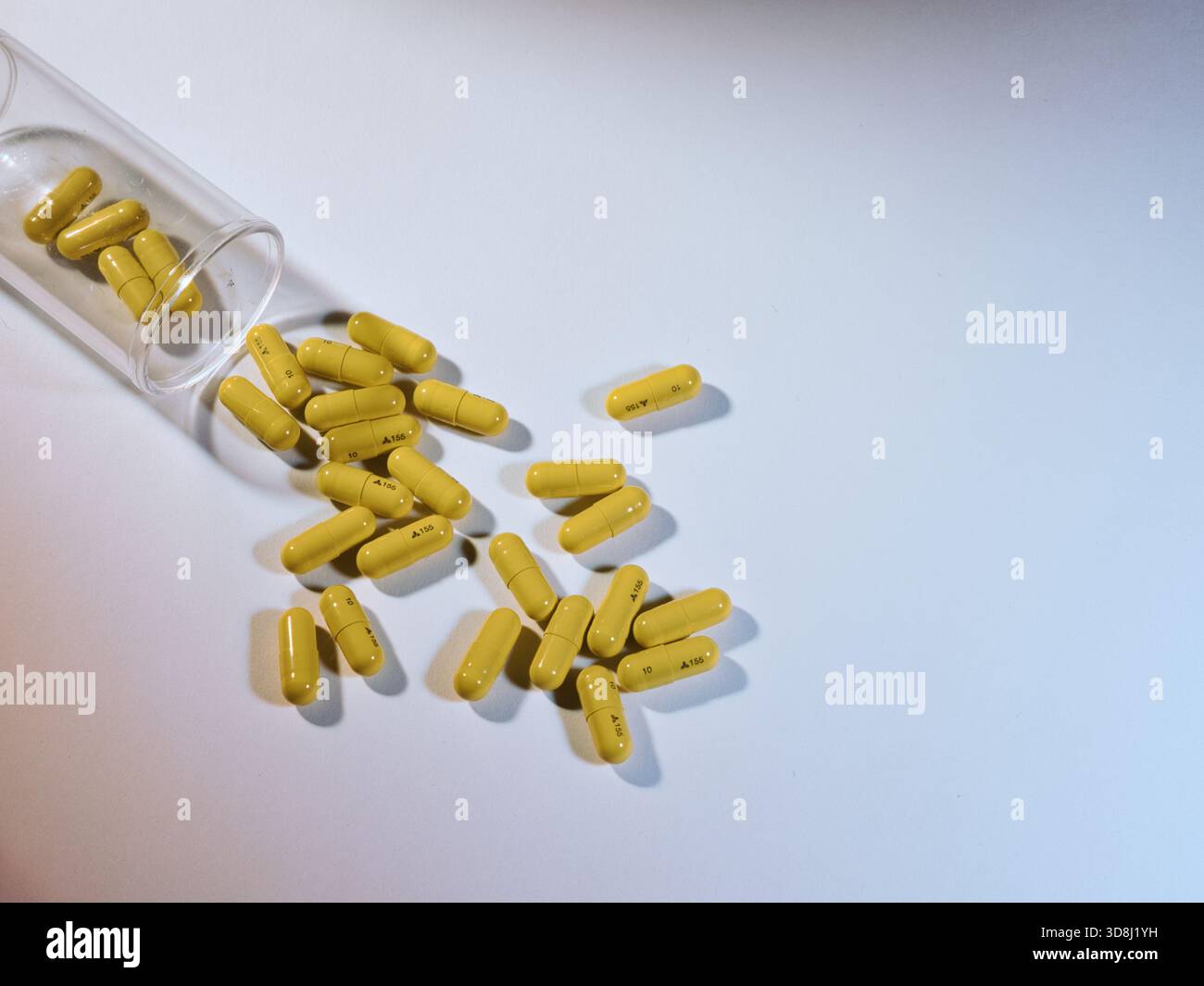 Capsule di medicina gialla - un colpo sopra di capsule di medicina gialla che fuoriescono da una bottiglia trasparente su una semplice superficie bianca, ideale per medici o Foto Stock