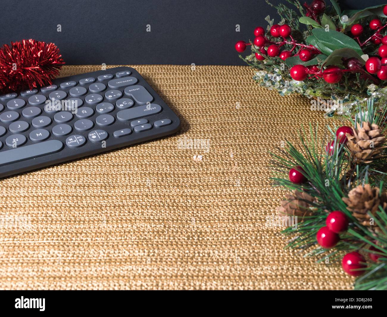Tema natalizio spazio di lavoro per le feste - tastiera moderna su una scrivania dorata con decorazioni natalizie: Bacche rosse, pinne e tinsel. Ideale per Foto Stock