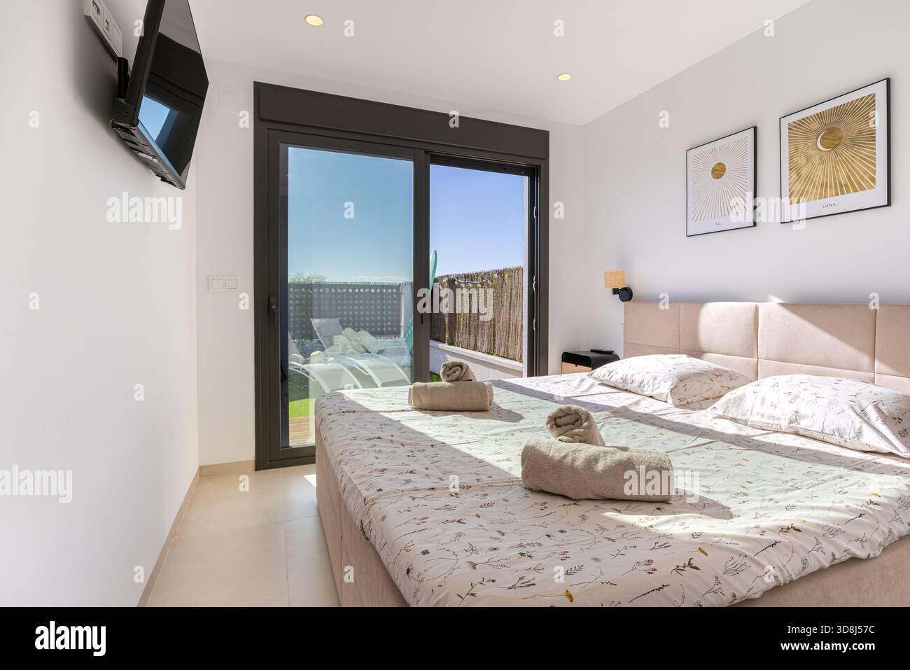 Camera soleggiata con soffici lenzuola floreali, TV e porte scorrevoli in vetro per la terrazza privata. Foto Stock