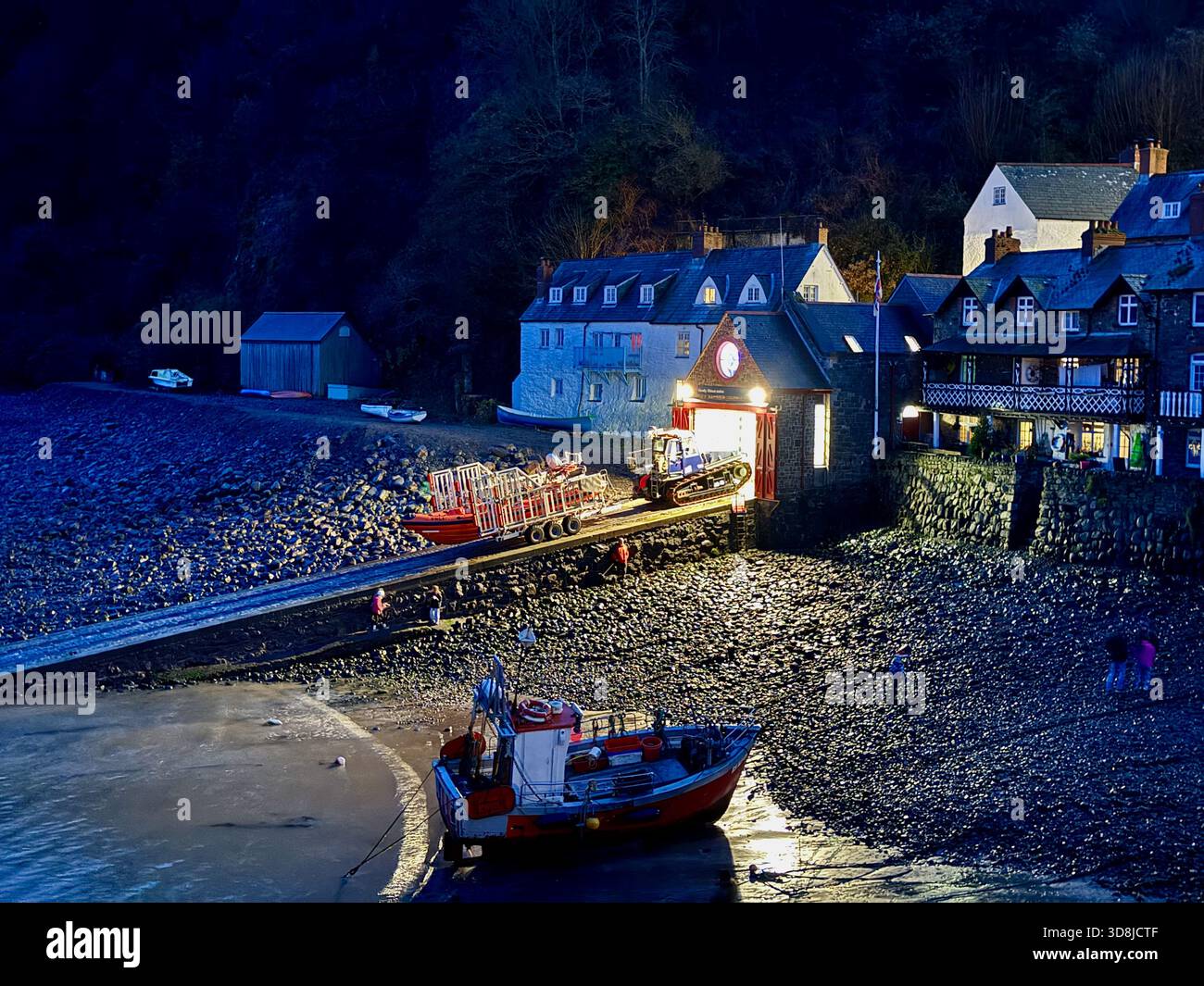 Stazione di salvataggio Clovelly RNLI al tramonto, sede della scialuppa di salvataggio costiera Toby Rundle, con scalo, trattore e barche sulla spiaggia di Devon. - Immagine stock catturata con smartphone