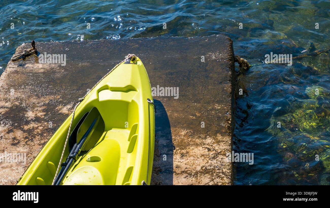 Un kayak giallo brillante si appoggia su un molo intempestivo in acque cristalline. Foto Stock