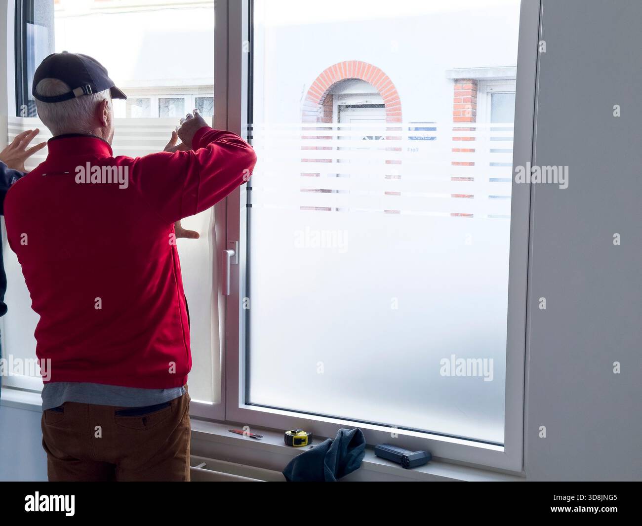 Lavoratore anziano che applica una pellicola traslucida per la privacy a una finestra Foto Stock