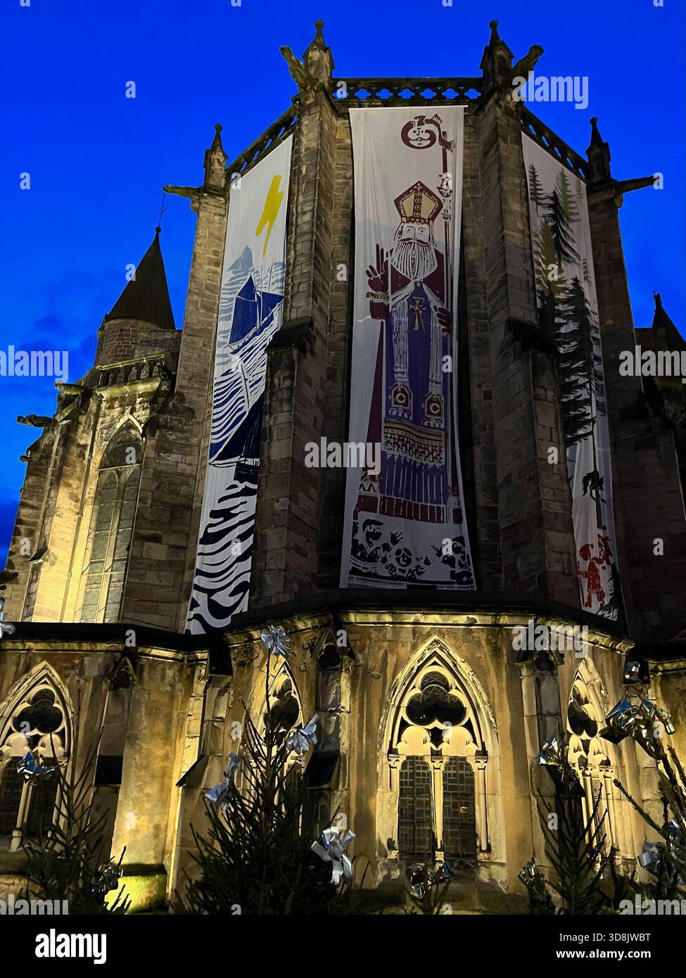Epinal, Francia – 21 dicembre 2024: Vista notturna della chiesa medievale con grandi striscioni illustrati e illuminazione architettonica colorata Foto Stock