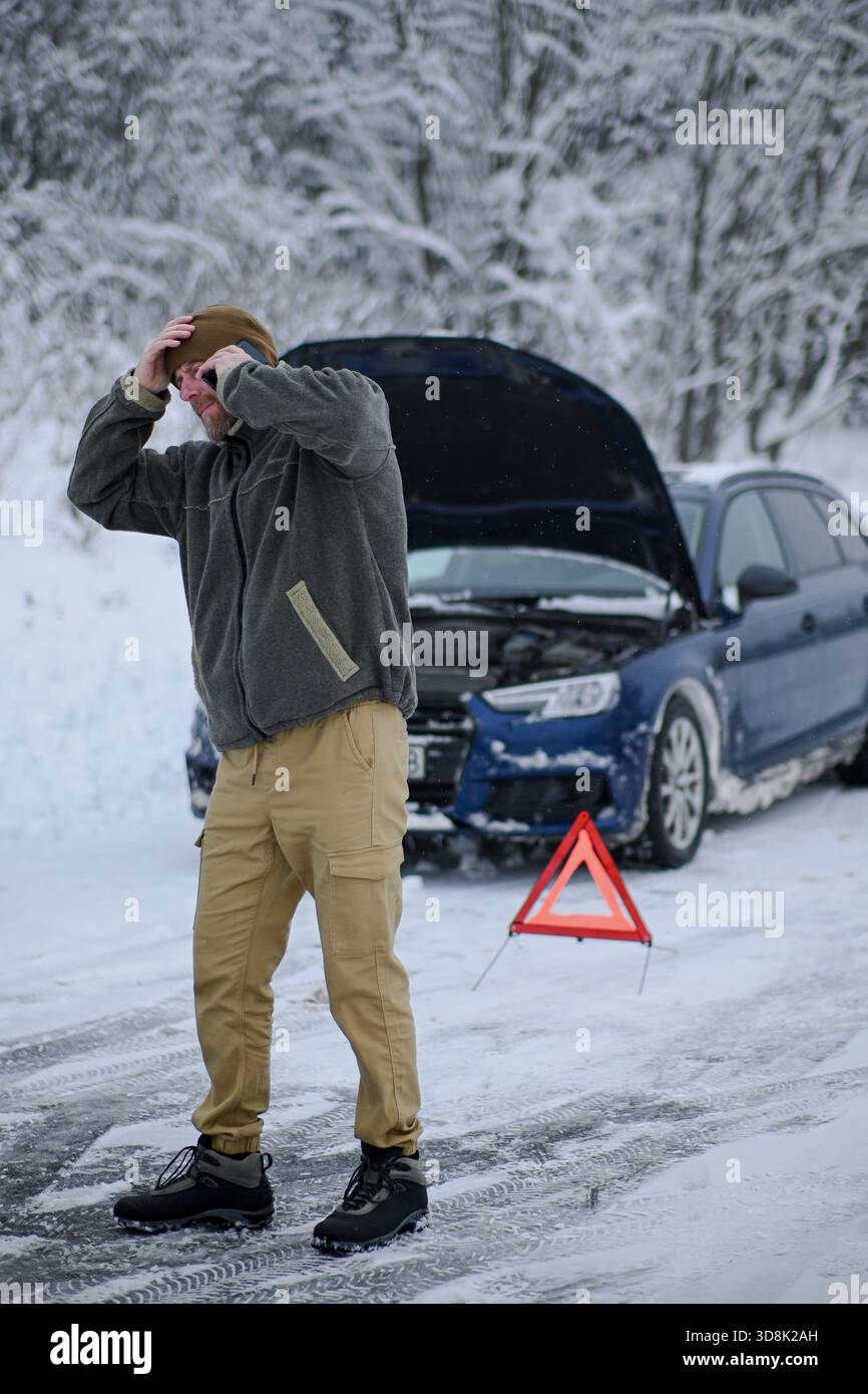 Uomo che in inverno si trova in difficoltà a causa di un guasto del veicolo e richiede assistenza stradale. Foto Stock