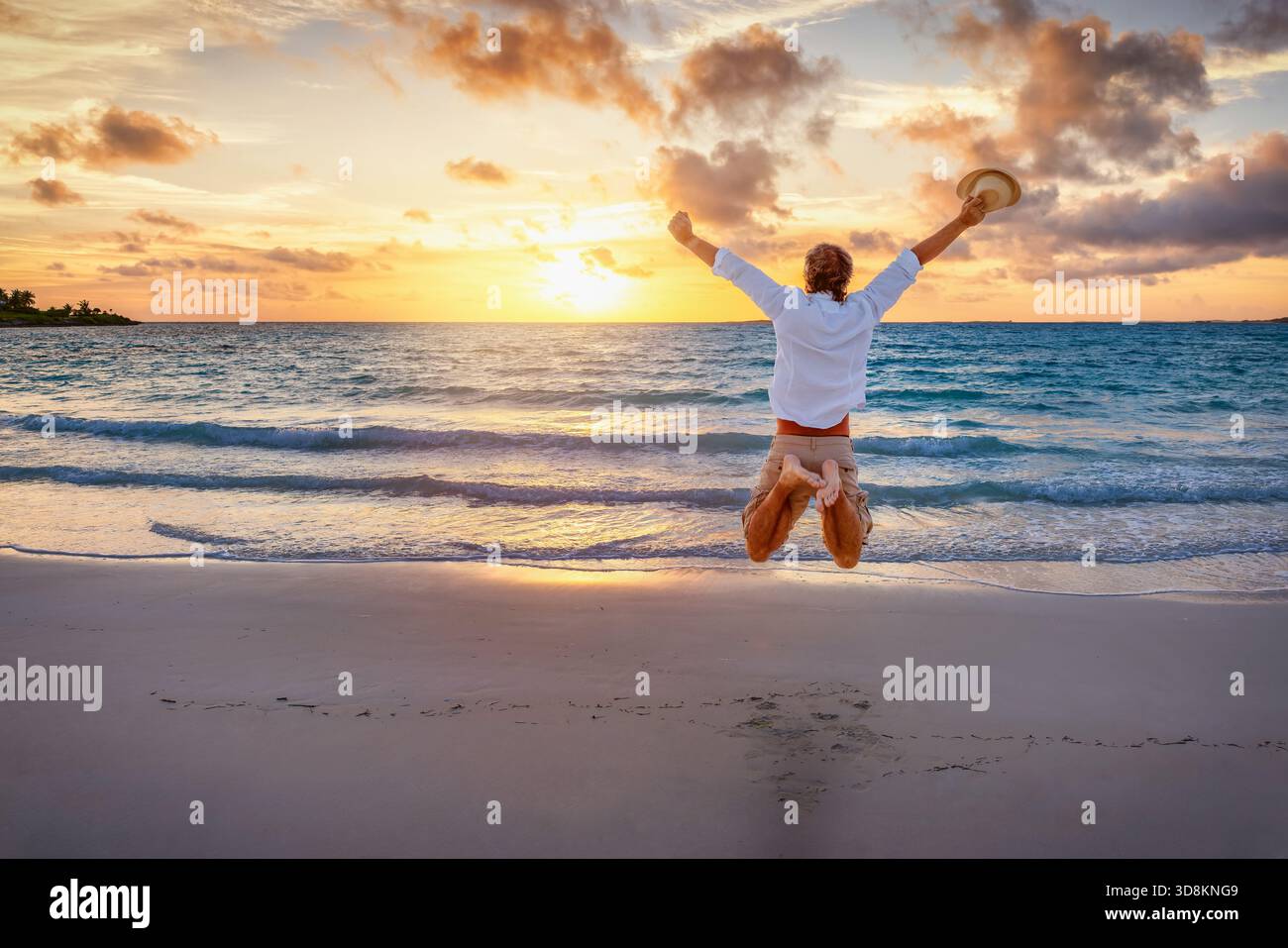 Un uomo felice salta in aria su una spiaggia tropicale paradisiaca durante l'alba o il tramonto come concetto di successo e felicità Foto Stock