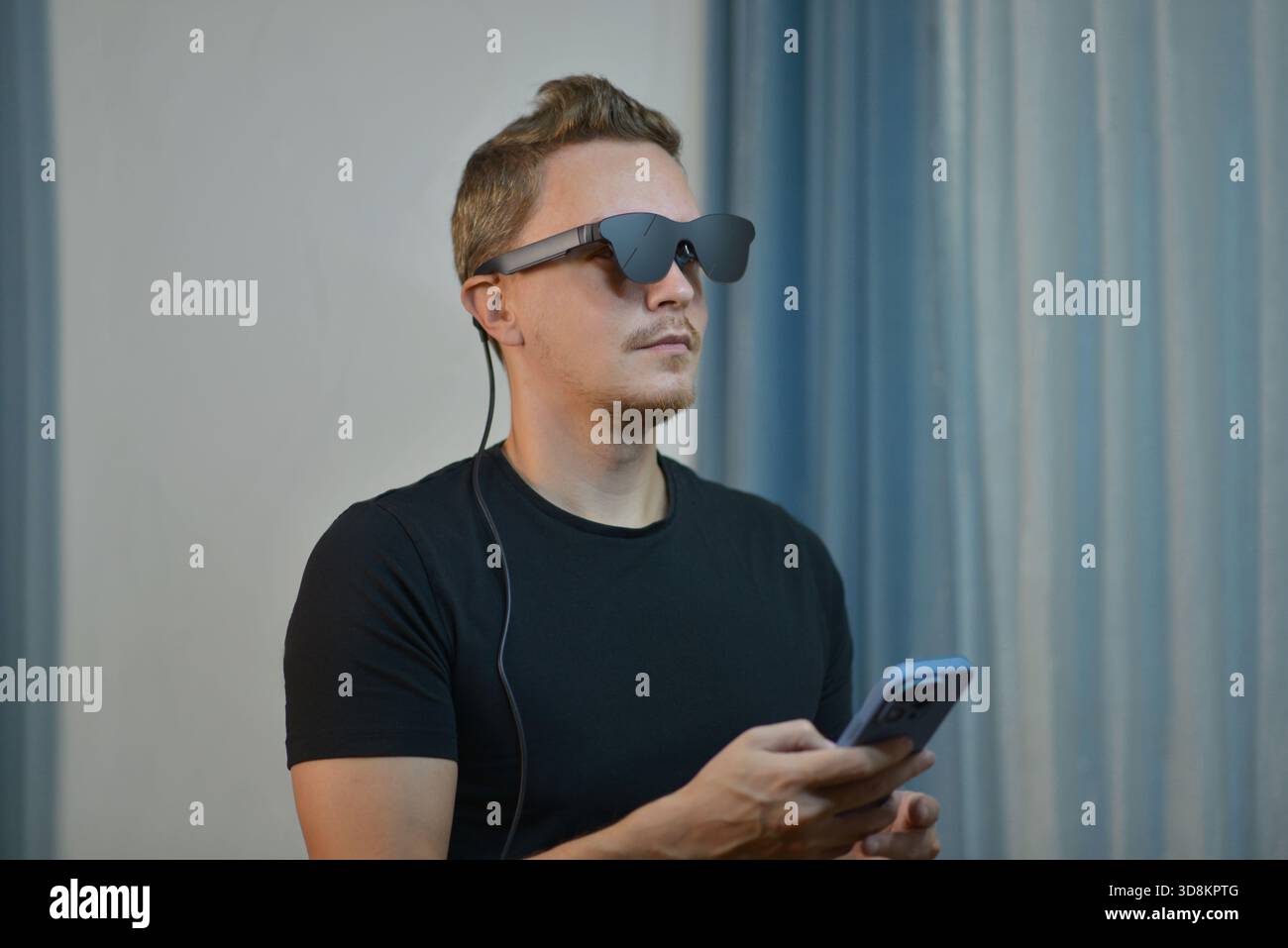 Un uomo che indossa occhiali AR moderni intelligenti connessi con lo smartphone. Tecnologia indossabile futuristica, occhiali digitali e gadget innovativi in un ambiente contemporaneo Foto Stock