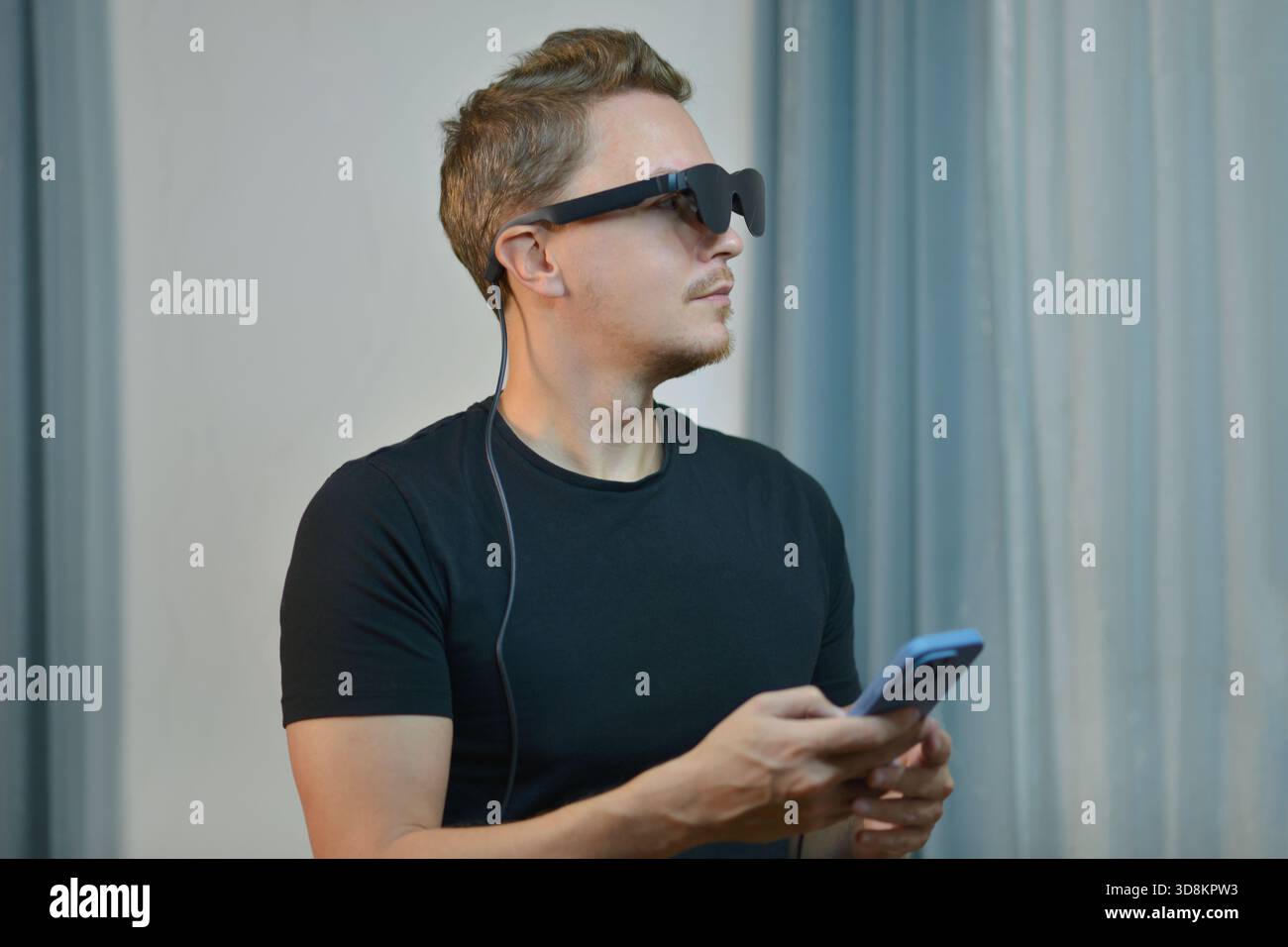 Un uomo che indossa occhiali AR moderni intelligenti connessi con lo smartphone. Tecnologia indossabile futuristica, occhiali digitali e gadget innovativi in un ambiente contemporaneo Foto Stock