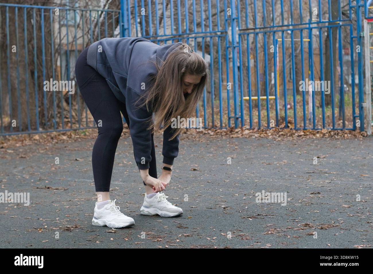 La giovane donna europea si piega in avanti e si allunga verso i piedi su campi sportivi all'aperto, routine di fitness, flessibilità, equilibrio, motivazione, benessere, guarigione Foto Stock