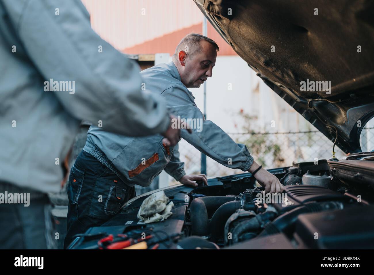 Due meccanici oggi ispezionano e riparano un veicolo sotto il cofano durante gli interventi di manutenzione all'aperto Foto Stock