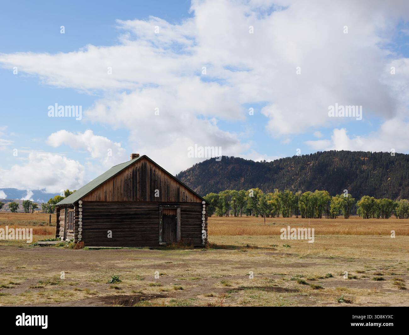 Semplice cabina esterna in legno su una vasta prateria autunnale con montagne boscose Foto Stock