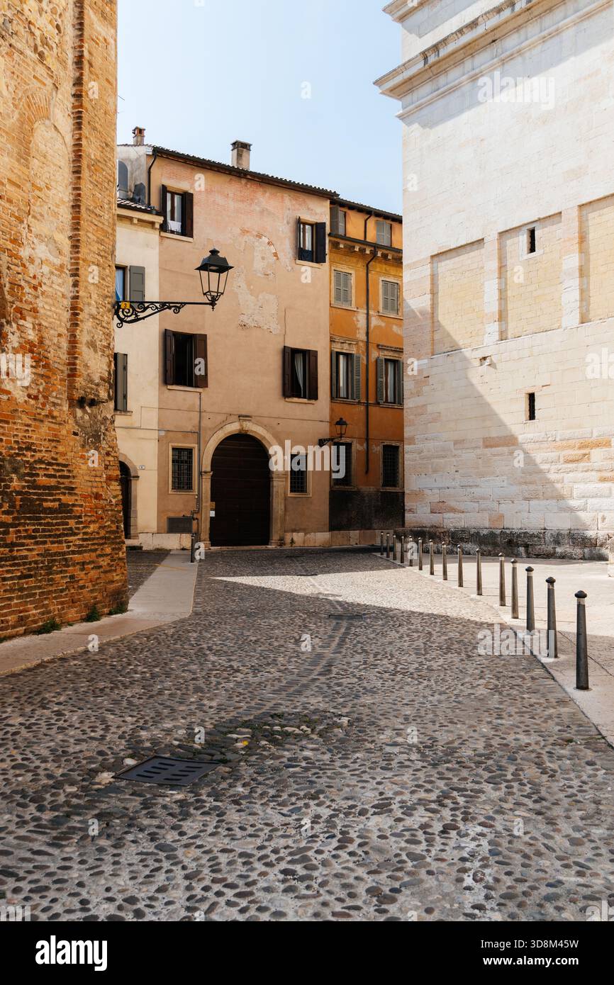 Un'affascinante strada acciottolata conduce ad un edificio a Verona, Italia, con dettagli architettonici e un'atmosfera soleggiata. Foto Stock