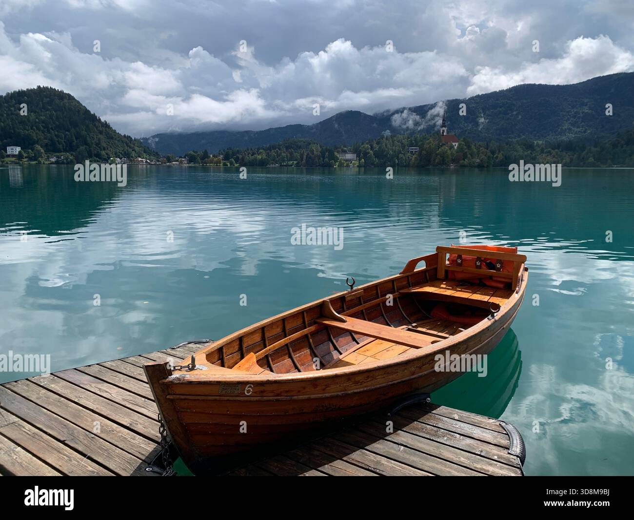 Momenti di bellezza catturando le acque cristalline, calme e turchesi del lago di Bled, in Slovenia, le barche a remi bilanciate sul bordo con vista sulle montagne - Immagine stock catturata con smartphone