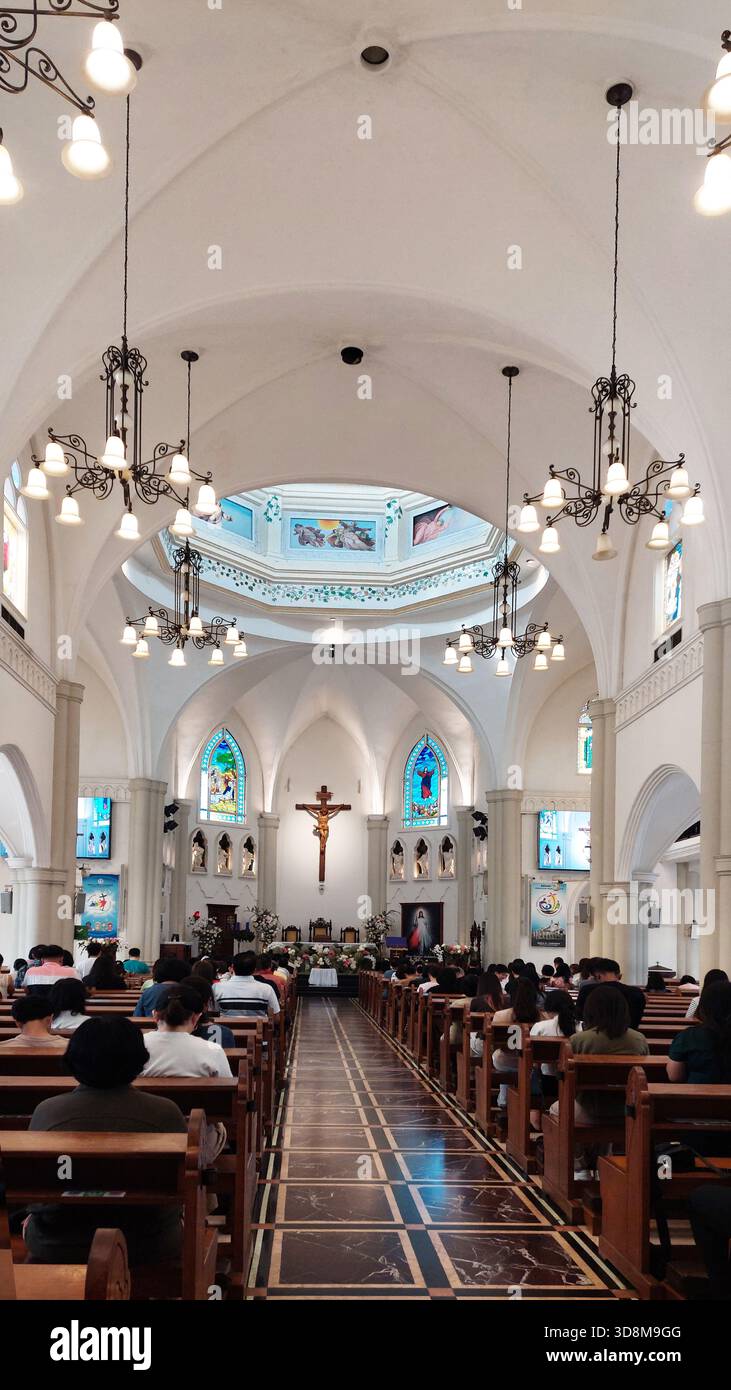 Eleganti interni della chiesa con vetrate colorate, lampadari e persone che assistono al servizio. Perfetto per temi di religione, culto, architettura, Foto Stock