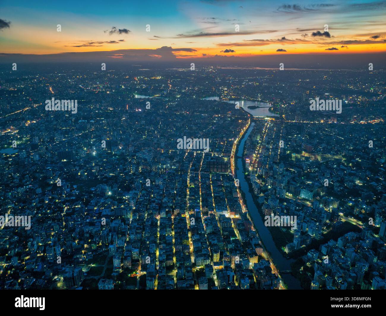 Vista aerea della città che si illumina di luci dorate lungo il canale sotto il cielo che svanisce al crepuscolo, Dacca, Divisione di Dacca, Bangladesh. Foto Stock