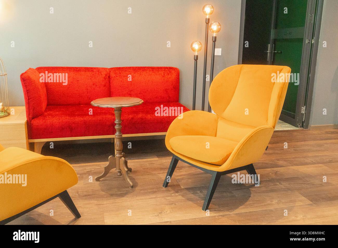 Un interno luminoso con un divano rosso e sedie gialle crea un'atmosfera lounge calda e moderna. Pavimenti in legno, illuminazione soffusa e arredi semplici Foto Stock