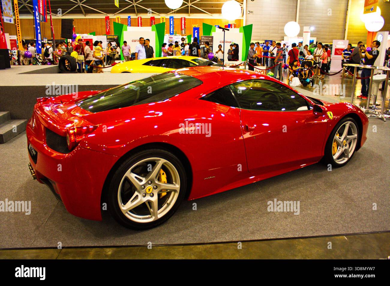 Le curve lucide e cremisi Ferrari 458 Italia dominano la sala espositiva con pavimento grigio lucido e sfondo tecnico Foto Stock