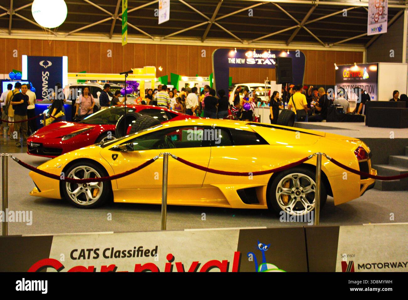 Un'elegante auto sportiva gialla è al centro di una vivace esposizione di automobili, circondata da folle e moderne esposizioni automobilistiche. Foto Stock